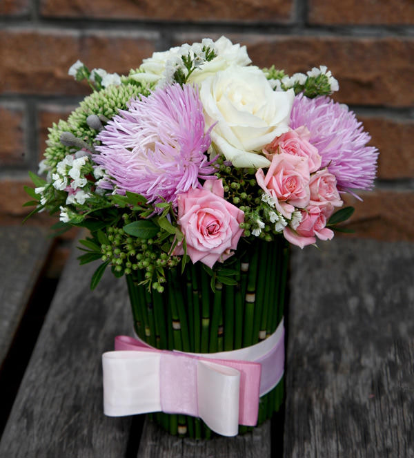 Интересная цветочная композиция из сиреневых астр, белых и розовых роз, оформленная милым бантом.