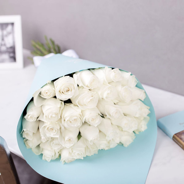 Закажите цветы на дом – букет роскошных белых роз в голубой крафтовой бумаге смотрится восхитительно.
